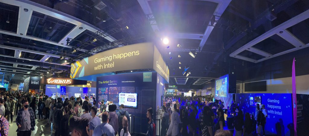 large convention expo room with vendor booths. booth text includes "Intel", "Aorus", and "Gaming happens with Intel." Crowds of people are seen in the foreground