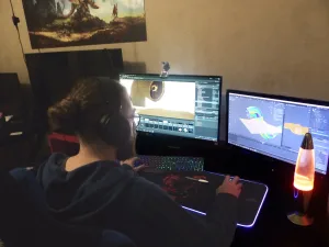 A man sits at his computer desk with two monitors in front of him.